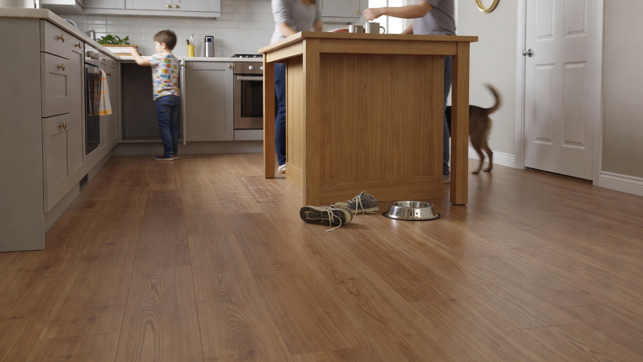 photorealistic wide shot of a busy family kitchen with AC4-rated medium-tone laminate flooring, children’s sneakers and a dog bowl visible near an island, natur